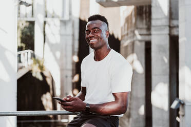 Male athlete using smart phone looking away while sitting - EBBF01357