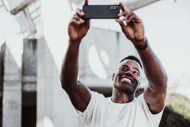 Lächelnder männlicher Sportler, der ein Selfie mit seinem Smartphone macht - EBBF01358