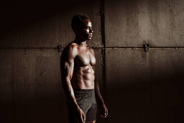 Sportsman with bare chested standing against gray wall during sunset - EBBF01365