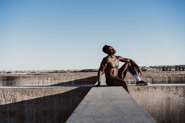 Betrachtung eines männlichen Sportlers an der Wand sitzend vor blauem Himmel - EBBF01377