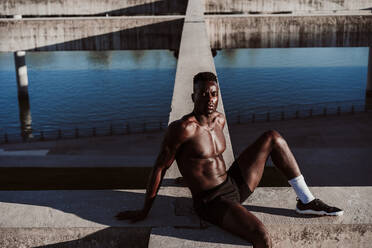 Young sportsman sitting on wall during sunny day - EBBF01378