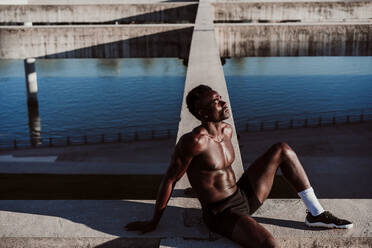 Thoughtful sportsman sitting on wall during sunny day - EBBF01379