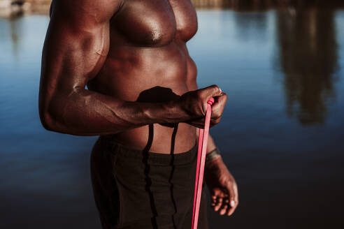 Sportsman pulling resistance band while standing against sea - EBBF01390