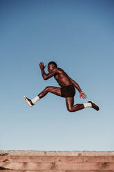 Young sportsman jumping over steps by clear sky during sunset - EBBF01396