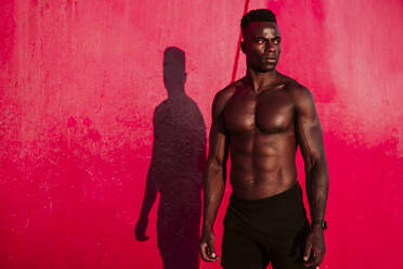 Male athlete standing against red wall during sunset - EBBF01398