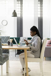 Woman writing in notepad while studying through laptop at home - GIOF09594