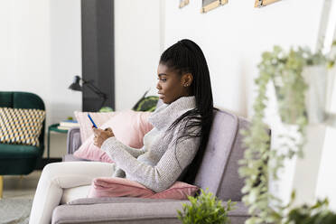 Junge Frau benutzt ihr Smartphone, während sie zu Hause auf dem Sofa im Wohnzimmer sitzt - GIOF09606