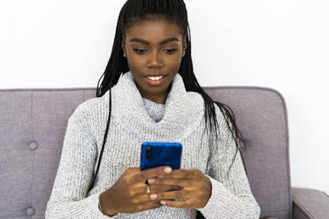 Woman text messaging on smart phone while sitting at home - GIOF09607