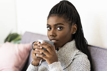 Woman drinking coffee while sitting on sofa in living room at home - GIOF09613