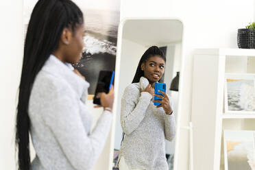 Young woman taking selfie through mirror reflection at home - GIOF09616