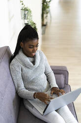Junge Frau arbeitet am Laptop, während sie zu Hause im Wohnzimmer sitzt - GIOF09618