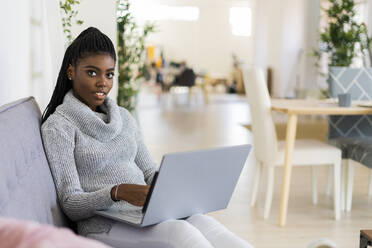 Unternehmerin arbeitet am Laptop, während sie zu Hause auf dem Sofa sitzt - GIOF09619