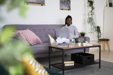 Businesswoman looking away while using laptop while sitting on sofa at home - GIOF09621