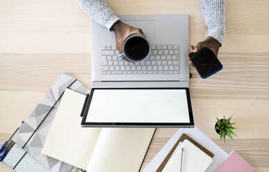 Hands of female freelancer holding coffee cup and smart phone while studying at home - GIOF09632