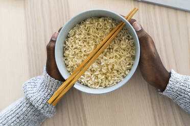 Hands of female holding noodle bowl at home - GIOF09634