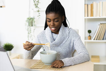 Junge Frau isst Nudeln, während sie zu Hause sitzt - GIOF09635