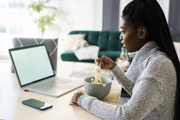 Frau isst Nudeln, während sie zu Hause am Laptop einen Film ansieht - GIOF09638