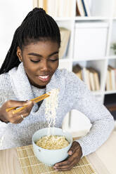 Frau isst Nudeln mit Stäbchen, während sie zu Hause sitzt - GIOF09643