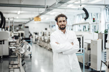 Male scientist wearing lab coat while standing with arms crossed at bright laboratory - JOSEF02147