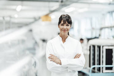 Smiling female scientist standing with arms crossed in bright laboratory - JOSEF02150