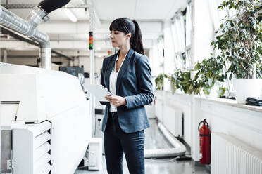 Businesswoman investigating while looking at machinery and holding digital tablet in industry - JOSEF02156