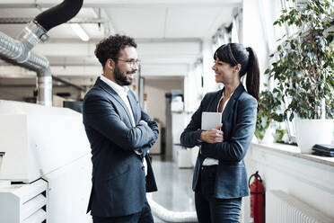 Smiling male and female business colleagues discussing while standing at bright industry - JOSEF02159