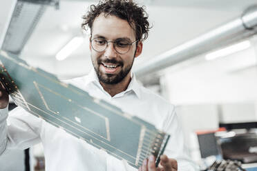 Lächelnder männlicher Ingenieur, der einen großen Computerchip in der Industrie untersucht - JOSEF02161