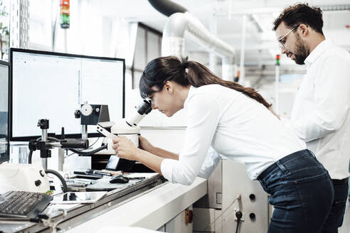 Weiblicher Techniker schaut durch ein Mikroskop, während er neben einem männlichen Kollegen im Labor steht - JOSEF02163