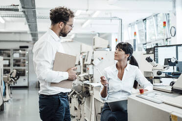 Confident female technician discussing with male colleague at laboratory - JOSEF02167