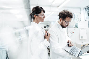 Eine Wissenschaftlerin steht neben einem männlichen Kollegen, der einen Laptop im Labor benutzt - JOSEF02174