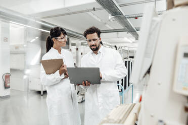 Eine Wissenschaftlerin sieht einen männlichen Kollegen an, der einen Laptop im Labor benutzt - JOSEF02175