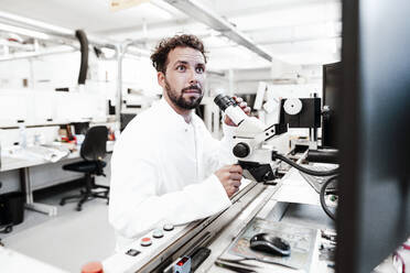 Male scientist sitting by microscope at bright laboratory - JOSEF02179