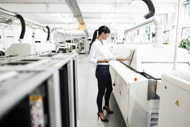Businesswoman examining machinery while holding digital tablet in industry - JOSEF02185