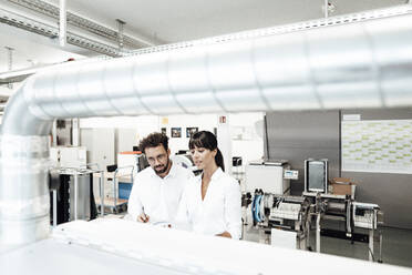 Female and male technicians investigating machinery at laboratory - JOSEF02186