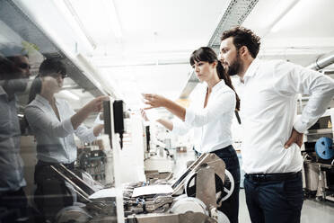 Male and female engineers looking at paper while investigating machinery in manufacturing industry - JOSEF02192