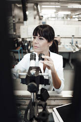 Female technician sitting with microscope at industry - JOSEF02196