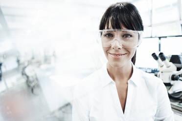 Smiling female technician wearing protective eyewear in industry - JOSEF02200