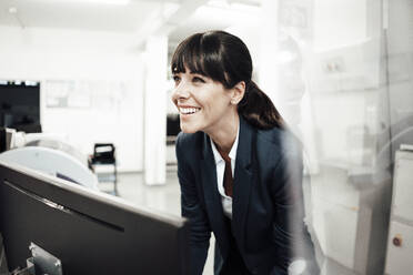 Fröhliche Geschäftsfrau schaut weg, während sie vor einem Computermonitor in der Industrie steht - JOSEF02204