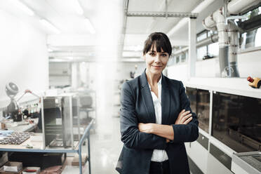 Confident businesswoman smiling while standing with arms crossed at industry - JOSEF02207