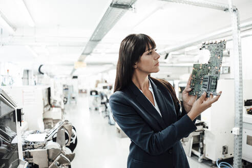 Businesswoman investigating while looking at circuit board in industry - JOSEF02210