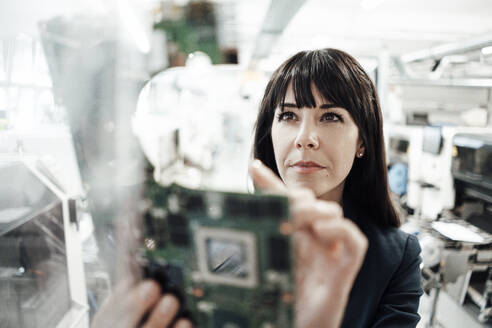 Confident female professional investigating while looking at circuit board in industry - JOSEF02211