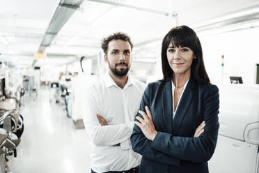 Confident businesswoman and male colleague standing with arms crossed at industry - JOSEF02215