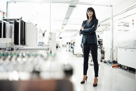 Confident mature businesswoman standing with arms crossed at industry stock photo