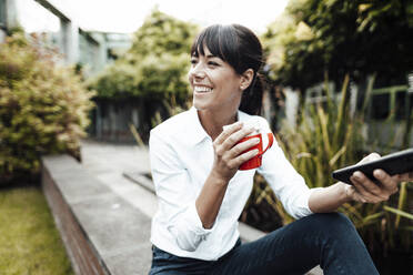 Smiling female professional holding coffee cup and smart phone while looking away - JOSEF02234