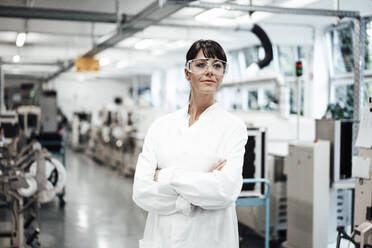 Confident female scientist standing with arms crossed while looking away in bright laboratory - JOSEF02244