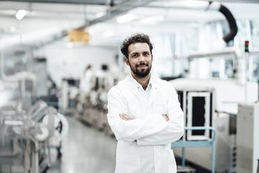 Confident male scientist in white lab coat while standing with arms crossed at bright laboratory - JOSEF02245