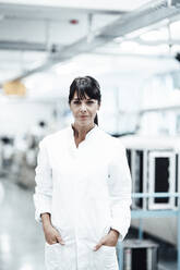 Confident female scientist standing with hands in pockets in bright laboratory - JOSEF02250