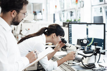 Weiblicher Geschäftsmann schaut durch ein Mikroskop, während er neben einem männlichen Kollegen im Labor steht - JOSEF02267