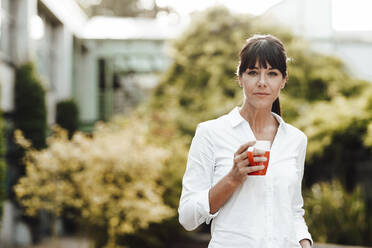 Selbstbewusste reife Geschäftsfrau, die eine Kaffeetasse hält, während sie vor Pflanzen steht - JOSEF02292