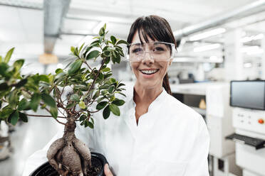 Smiling female scientist holding potted plant at laboratory - JOSEF02299